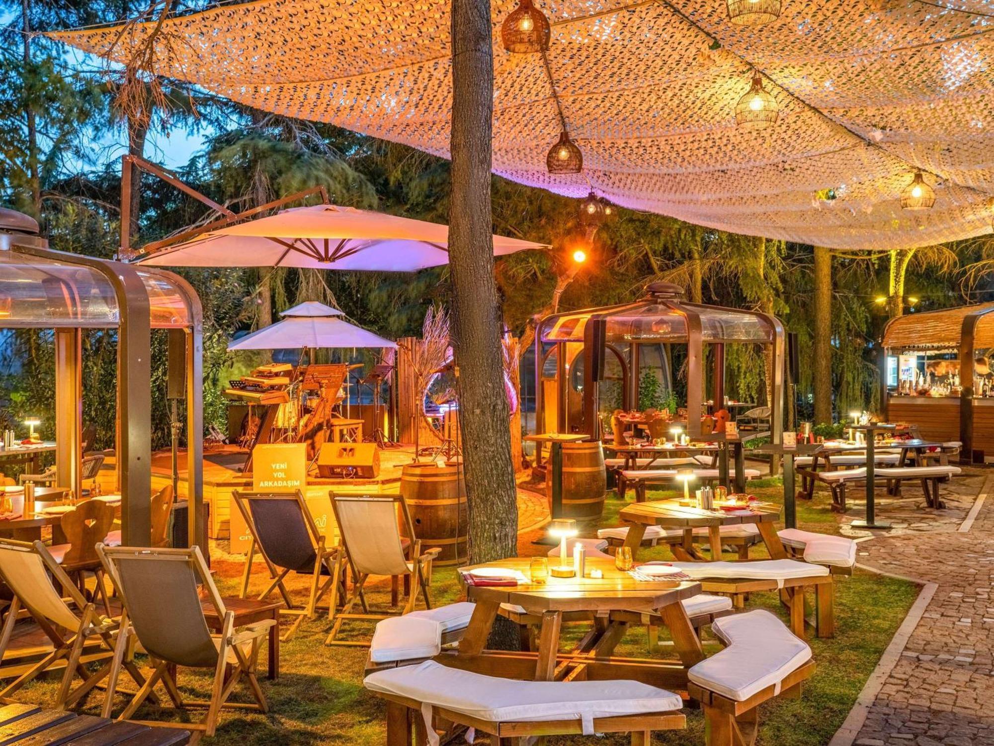 Swissotel The Bosphorus Istanbul Luaran gambar The photo depicts a beautifully arranged outdoor dining space. There are wooden tables and chairs arranged across a grassy area, some featuring cozy seating. Large umbrellas provide shade, and there are unique, transparent structures, possibly for di