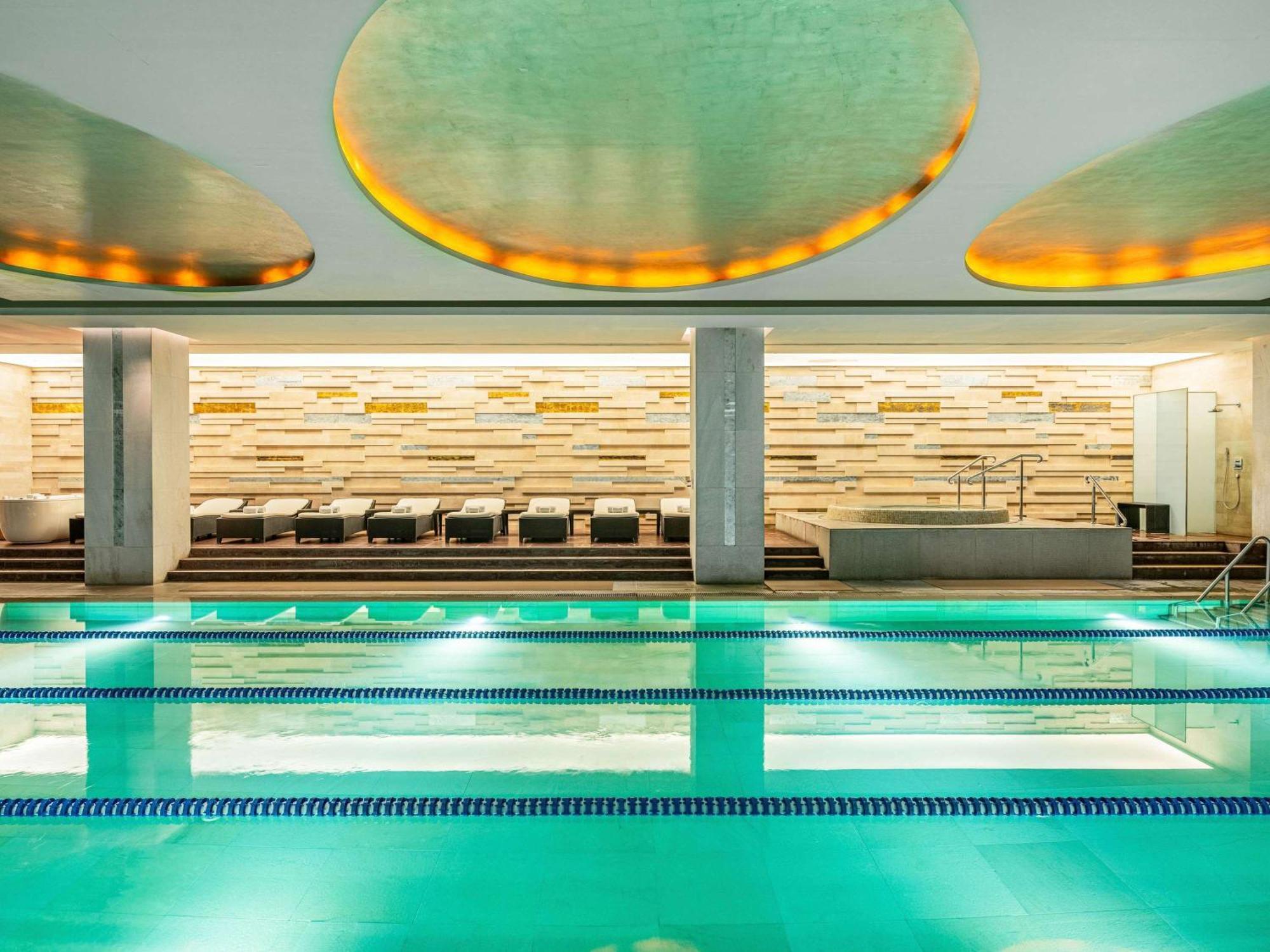 Swissotel The Bosphorus Istanbul Luaran gambar The photo shows an indoor swimming pool area. The pool has a calm, turquoise water and is bordered by a sleek tiled edge. Above the pool, there are large, circular ceiling features with soft lighting casting a warm glow. In the background, there's a 