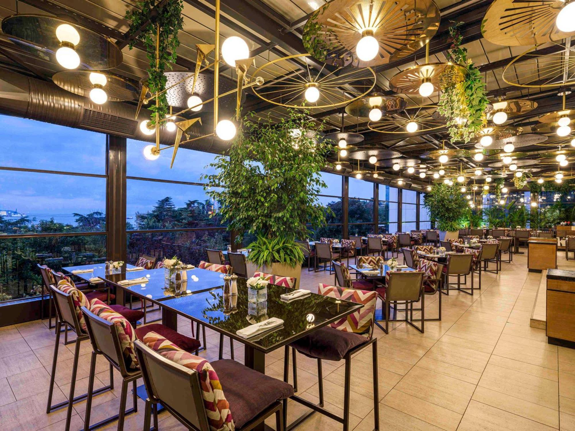 Swissotel The Bosphorus Istanbul Luaran gambar The photo shows a stylish restaurant interior with a modern design. It features several long tables with chairs arranged neatly. The atmosphere is enhanced by large windows that provide a view of the outside. The ceiling is adorned with unique light 