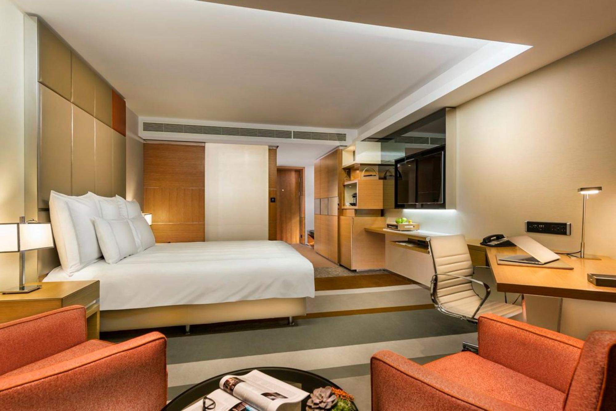 Swissotel The Bosphorus Istanbul Luaran gambar The photo shows a modern hotel room featuring a comfortable king-sized bed with white bedding. There are two bright orange armchairs positioned beside a round coffee table that holds a magazine. The room has a contemporary design, with light wood acc