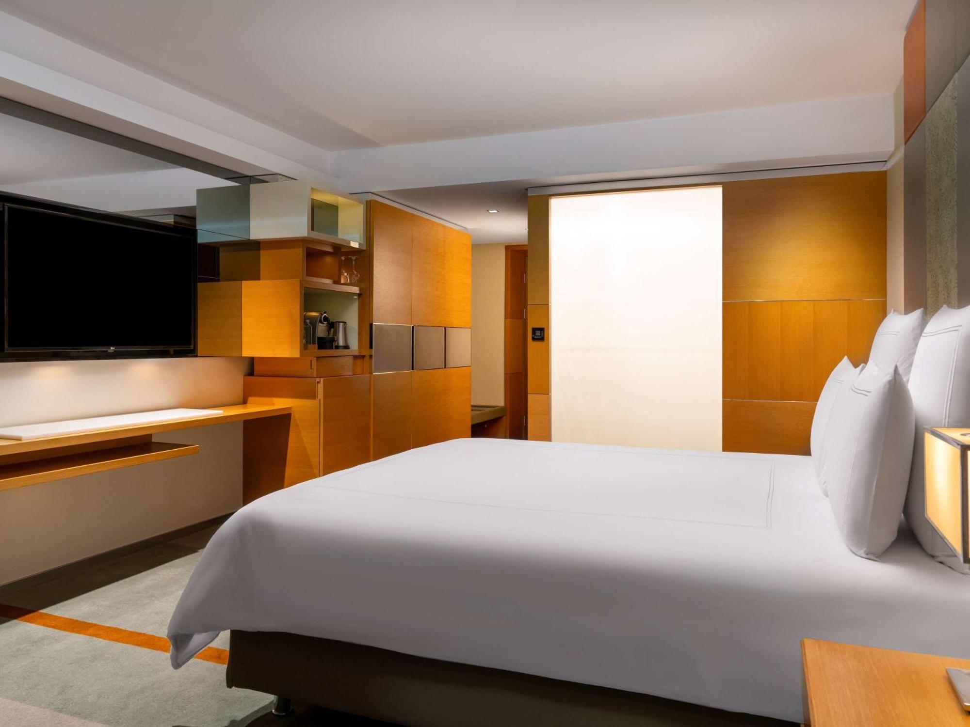 Swissotel The Bosphorus Istanbul Luaran gambar The photo shows a modern hotel room. It features a large bed with white linens and pillows at the forefront. The walls and furniture have a warm, wooden finish, giving the space a cozy and contemporary feel. To one side, there is a flat-screen televi
