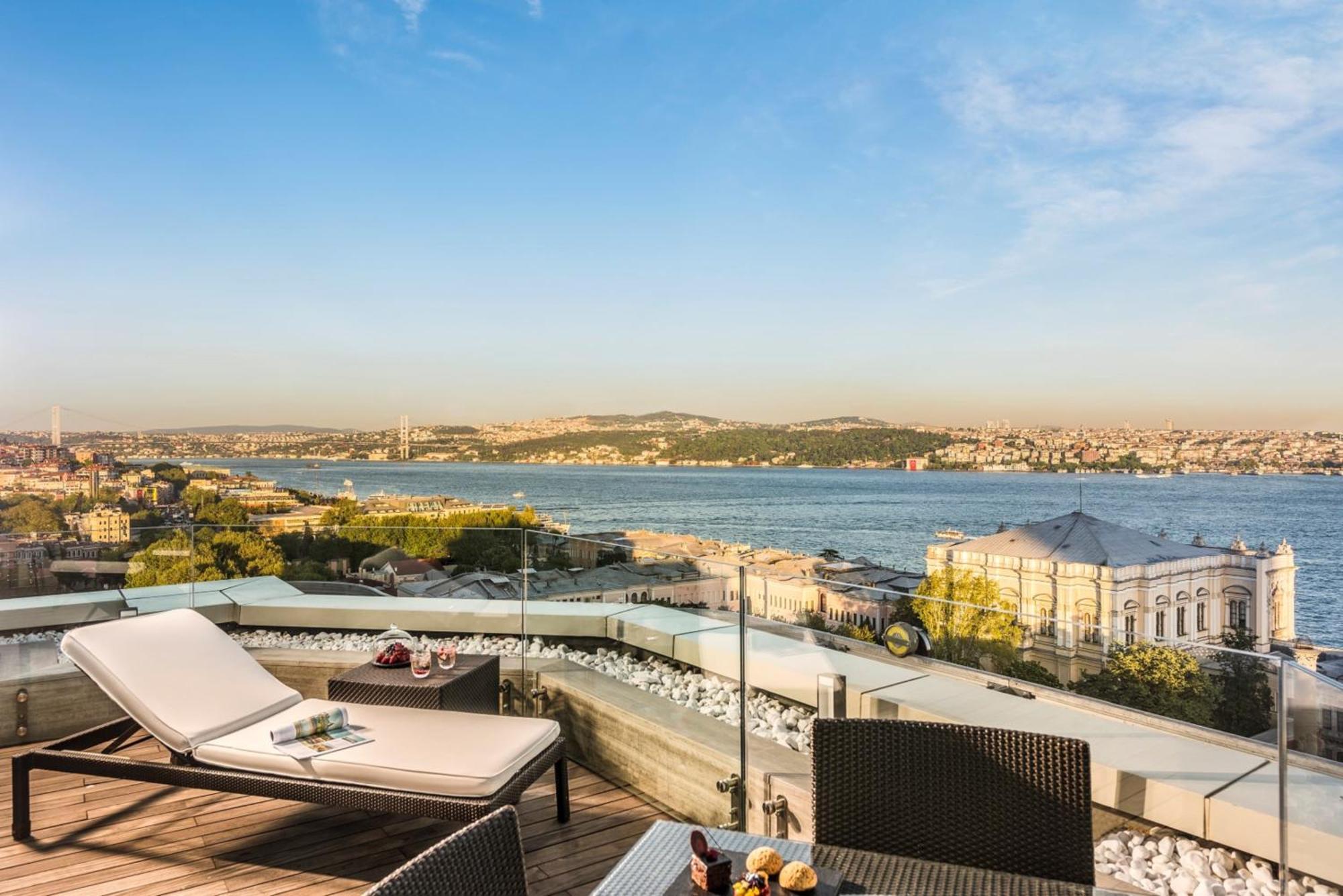 Swissotel The Bosphorus Istanbul Luaran gambar The photo shows a scenic view from a balcony or terrace overlooking a river or body of water. There are two lounge chairs positioned on the deck, surrounded by a modern and stylish setup featuring a small table. The landscape includes distant hills o