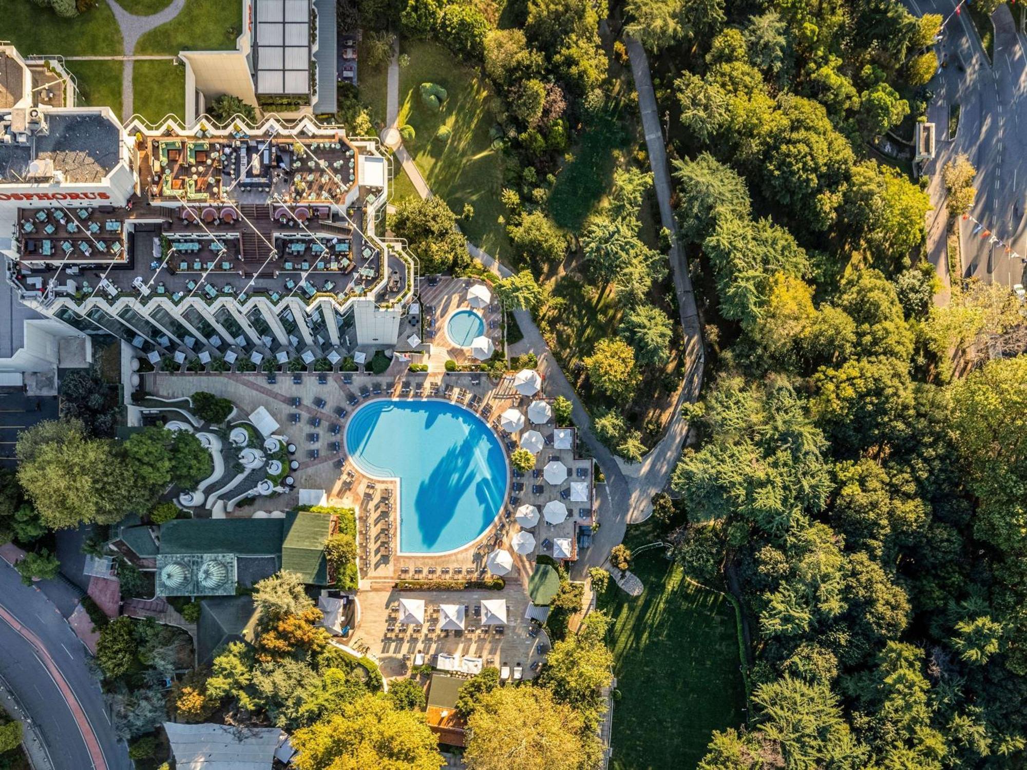 Swissotel The Bosphorus Istanbul Luaran gambar The photo shows an aerial view of a hotel complex surrounded by lush greenery. In the center, there is a large, blue swimming pool, with several lounge chairs arranged around it. The hotel building has a modern architectural design, featuring multipl